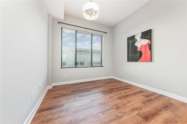 spare room with an inviting chandelier and wood-type flooring