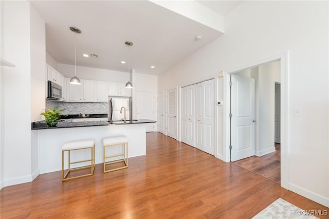 kitchen with decorative light fixtures, white cabinets, decorative backsplash, fridge, and kitchen peninsula