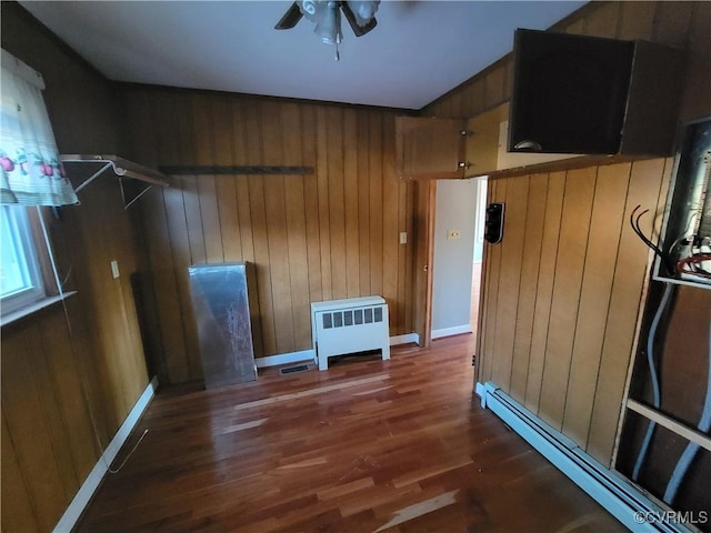 interior space with ceiling fan, wood walls, dark hardwood / wood-style floors, and a baseboard radiator