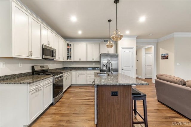 kitchen with appliances with stainless steel finishes, pendant lighting, white cabinetry, sink, and a kitchen island with sink