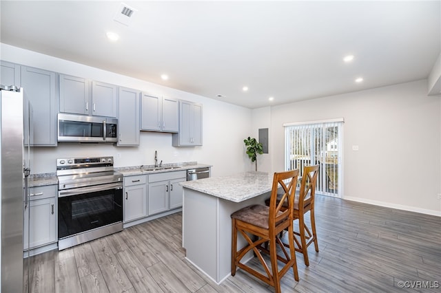 kitchen featuring a kitchen island, appliances with stainless steel finishes, sink, a kitchen breakfast bar, and light wood-type flooring