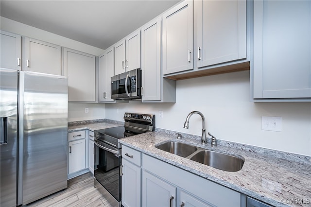 kitchen featuring light stone countertops, appliances with stainless steel finishes, sink, and light wood-type flooring