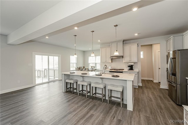 kitchen featuring dark wood-type flooring, stainless steel fridge, a breakfast bar, hanging light fixtures, and a center island with sink