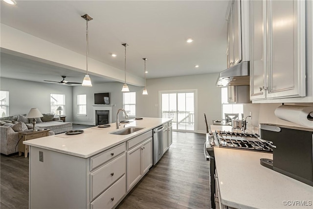 kitchen with sink, dark wood-type flooring, a kitchen island with sink, hanging light fixtures, and stainless steel appliances