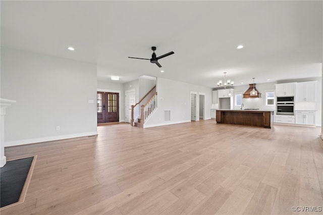 unfurnished living room with sink, ceiling fan with notable chandelier, and light hardwood / wood-style flooring