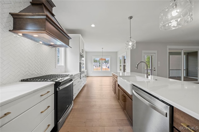 kitchen featuring appliances with stainless steel finishes, decorative light fixtures, white cabinetry, decorative backsplash, and custom exhaust hood