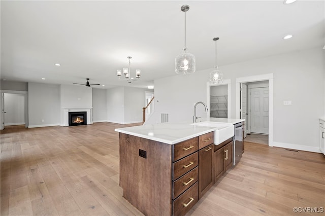 kitchen with sink, hanging light fixtures, light wood-type flooring, dishwasher, and a kitchen island with sink