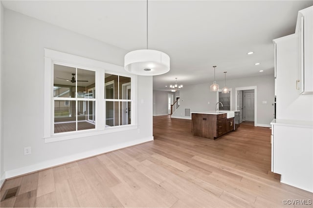 kitchen with ceiling fan with notable chandelier, pendant lighting, a kitchen island with sink, dark brown cabinetry, and light wood-type flooring