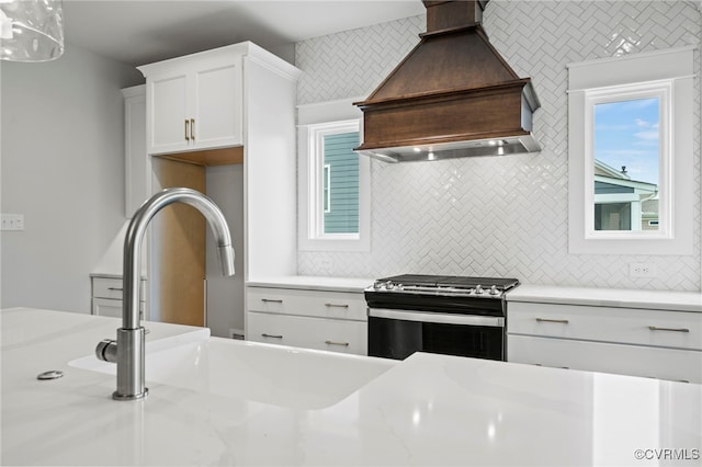 kitchen with premium range hood, white cabinetry, sink, decorative backsplash, and stainless steel gas range