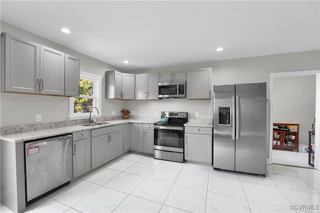 kitchen featuring light stone counters, stainless steel appliances, sink, and gray cabinetry