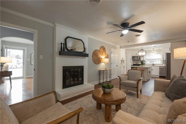 living room featuring ornamental molding, a wealth of natural light, a fireplace, and light hardwood / wood-style floors