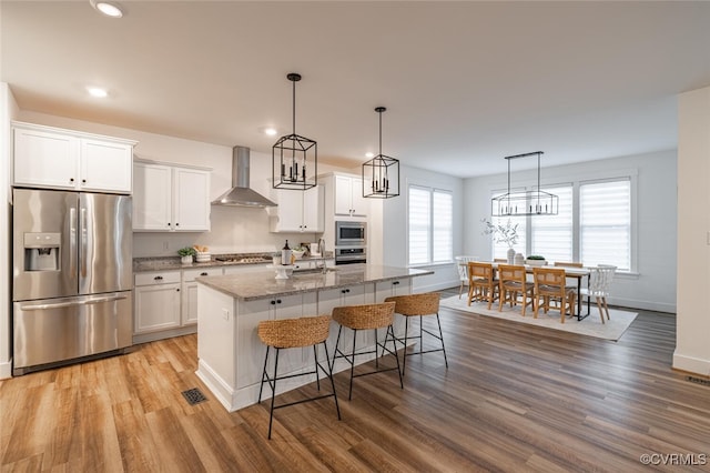 kitchen featuring stainless steel appliances, a kitchen island with sink, wall chimney range hood, and white cabinets