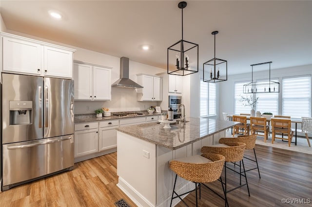 kitchen featuring appliances with stainless steel finishes, a kitchen island with sink, white cabinets, and wall chimney exhaust hood