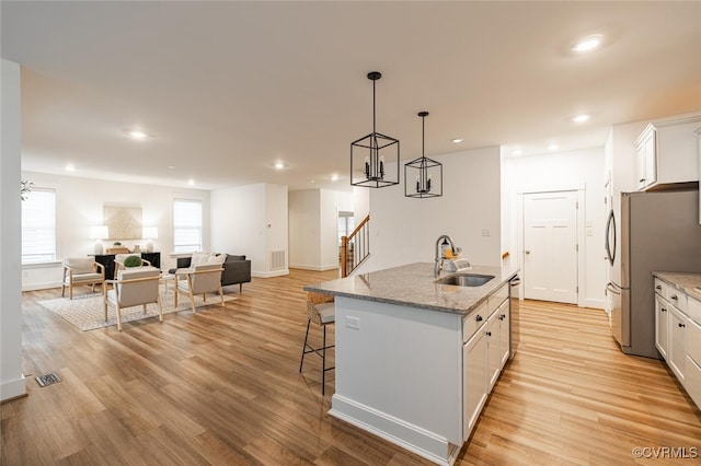 kitchen with white cabinetry, sink, hanging light fixtures, and a center island with sink