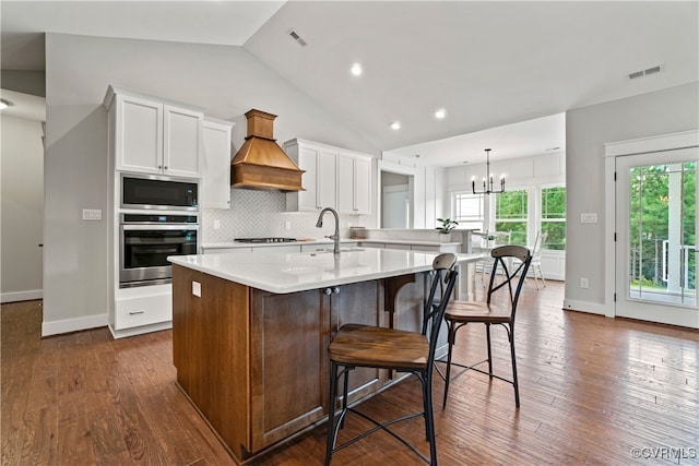 kitchen with premium range hood, a breakfast bar area, a center island with sink, appliances with stainless steel finishes, and white cabinets