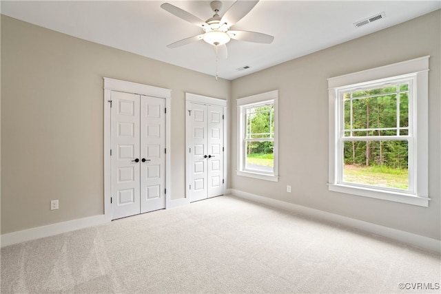 unfurnished bedroom with light carpet, two closets, and ceiling fan