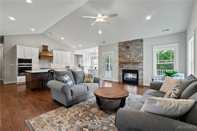 living room with a fireplace, ceiling fan with notable chandelier, vaulted ceiling, and dark hardwood / wood-style floors