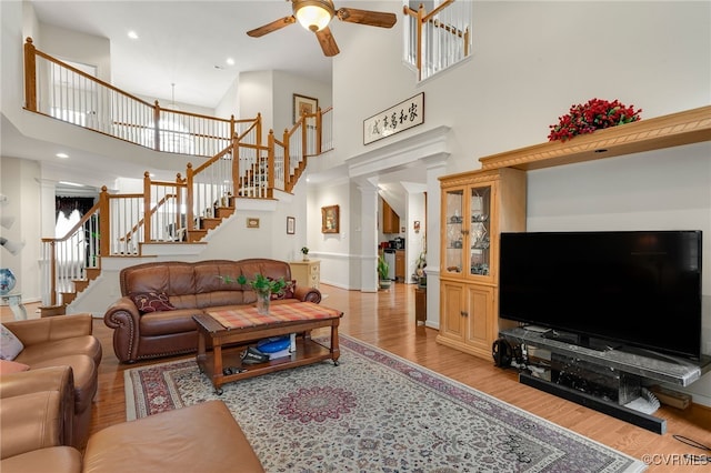 living room with ceiling fan, a high ceiling, and light wood-type flooring