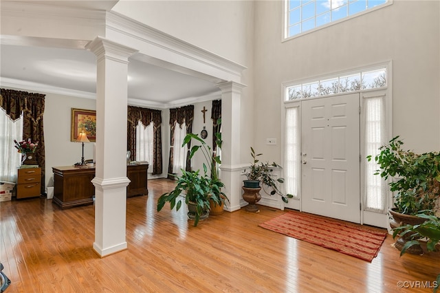 entrance foyer featuring crown molding, light hardwood / wood-style flooring, decorative columns, and a high ceiling