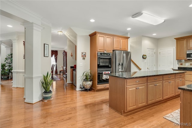 kitchen with ornate columns, appliances with stainless steel finishes, dark stone counters, a center island, and light hardwood / wood-style floors