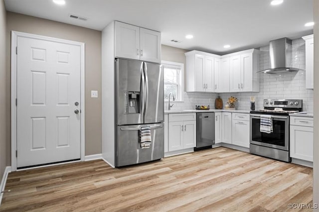 kitchen featuring wall chimney exhaust hood, white cabinetry, appliances with stainless steel finishes, and light hardwood / wood-style flooring