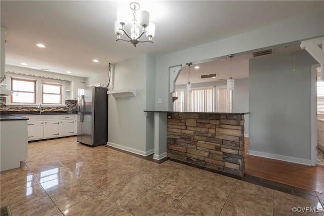 kitchen with white cabinetry, decorative light fixtures, a chandelier, stainless steel fridge, and backsplash