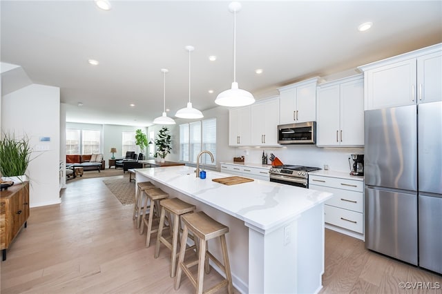 kitchen featuring decorative light fixtures, white cabinetry, a kitchen island with sink, light stone counters, and stainless steel appliances