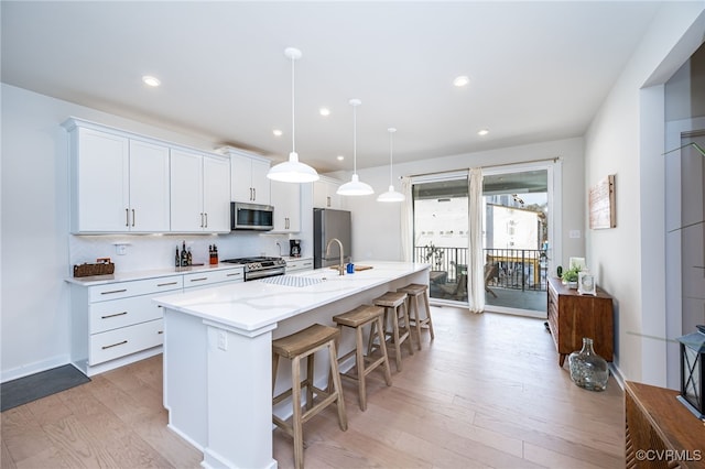 kitchen with pendant lighting, sink, appliances with stainless steel finishes, white cabinetry, and an island with sink