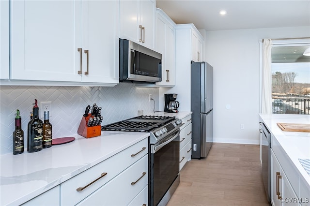 kitchen featuring white cabinetry, light stone counters, stainless steel appliances, light hardwood / wood-style floors, and decorative backsplash