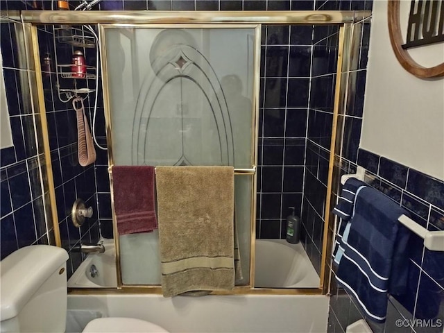 bathroom featuring tile walls, toilet, and combined bath / shower with glass door