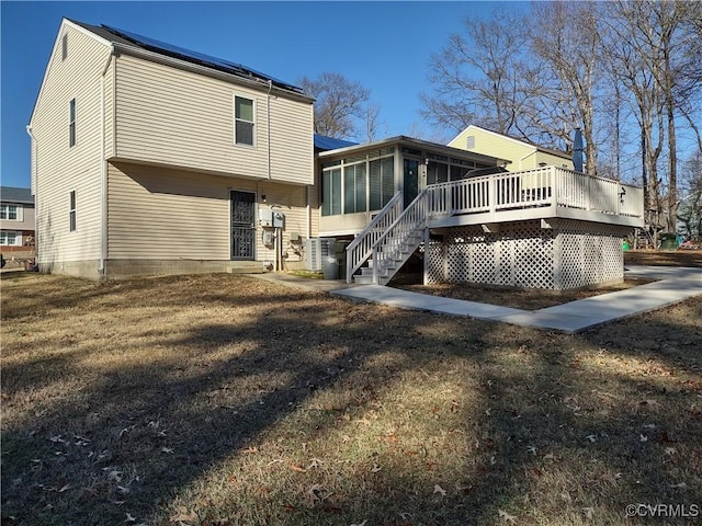 back of property with a wooden deck, a yard, and a sunroom