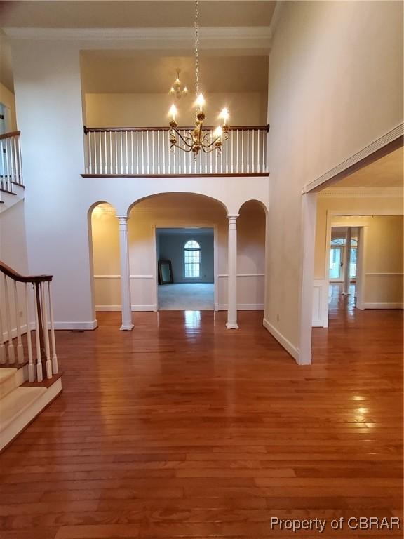 unfurnished living room with hardwood / wood-style floors, ornamental molding, and a high ceiling