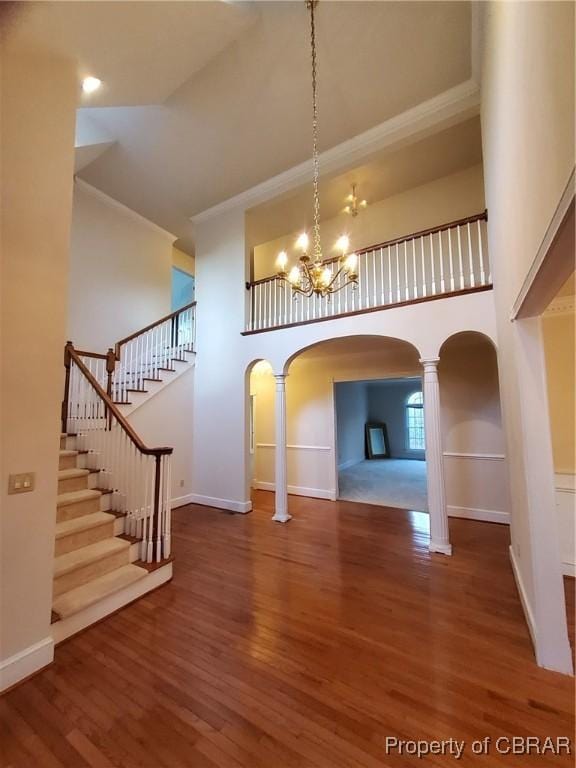 interior space with a towering ceiling, hardwood / wood-style floors, decorative columns, a notable chandelier, and crown molding