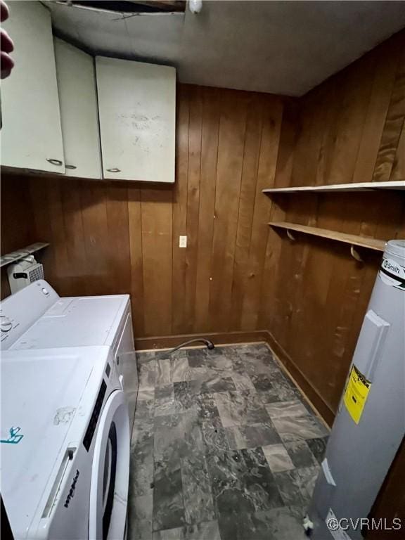 laundry room featuring cabinets, wood walls, washing machine and clothes dryer, and water heater