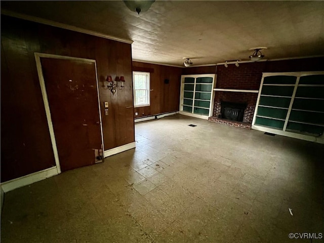 unfurnished living room featuring a fireplace, a baseboard radiator, ornamental molding, and wooden walls