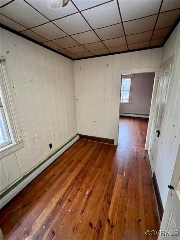 spare room with baseboard heating, a paneled ceiling, and wood-type flooring