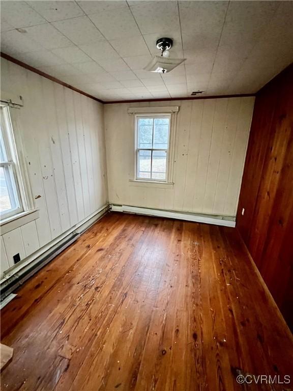 unfurnished room with hardwood / wood-style flooring, ornamental molding, wood walls, and baseboard heating