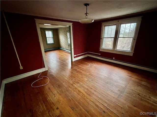 unfurnished dining area featuring crown molding, a baseboard heating unit, and hardwood / wood-style floors