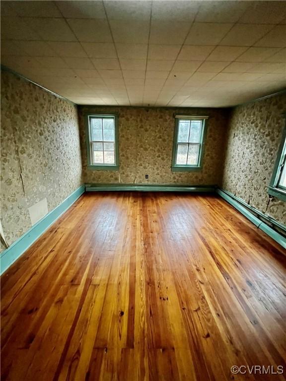 empty room with wood-type flooring, a healthy amount of sunlight, and a paneled ceiling