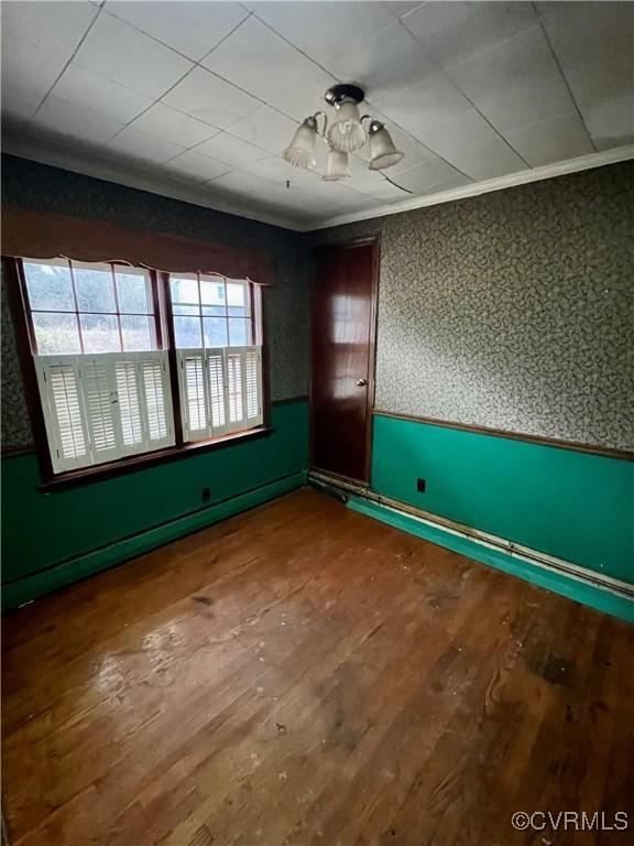 empty room featuring baseboard heating, ornamental molding, and hardwood / wood-style floors