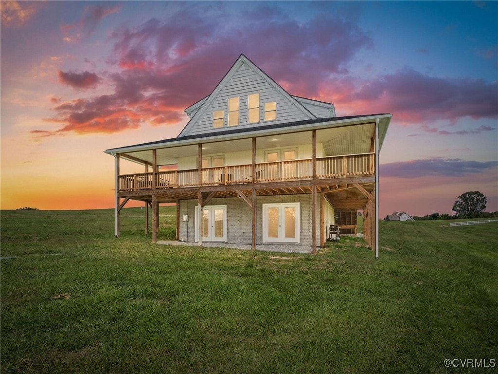 back house at dusk featuring a wooden deck and a lawn