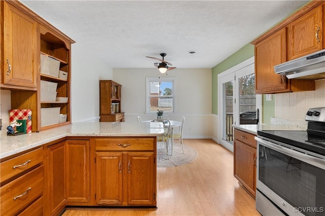 kitchen with light hardwood / wood-style flooring, light stone counters, tasteful backsplash, stainless steel range with electric cooktop, and kitchen peninsula