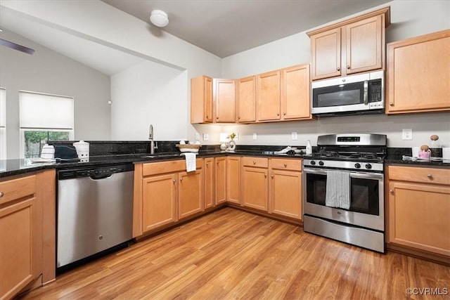 kitchen with sink, appliances with stainless steel finishes, vaulted ceiling, dark stone counters, and light wood-type flooring