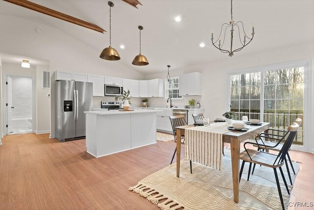 kitchen with a kitchen island, decorative light fixtures, white cabinetry, stainless steel appliances, and light hardwood / wood-style flooring