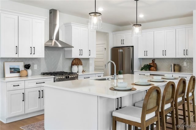 kitchen featuring sink, white cabinetry, a center island with sink, high quality appliances, and wall chimney range hood