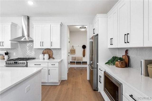 kitchen featuring white cabinetry, decorative backsplash, high end appliances, wall chimney range hood, and light wood-type flooring