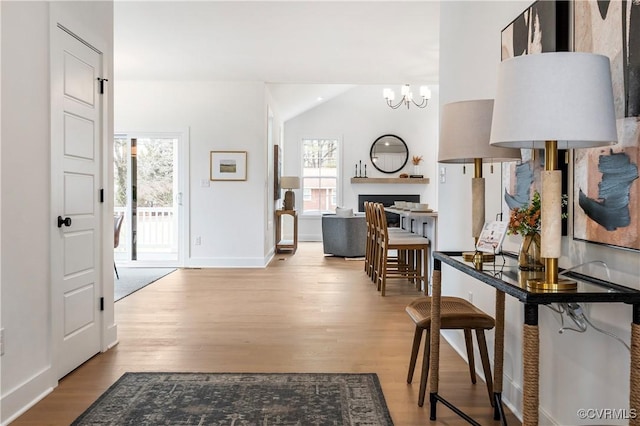 hall featuring lofted ceiling, an inviting chandelier, and light hardwood / wood-style flooring