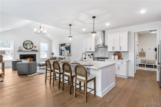 kitchen featuring pendant lighting, an island with sink, white cabinets, a kitchen bar, and wall chimney range hood