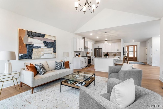 living room featuring vaulted ceiling, sink, a notable chandelier, and light wood-type flooring