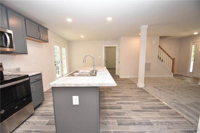 kitchen with sink, a kitchen island with sink, hardwood / wood-style floors, gray cabinetry, and stainless steel appliances